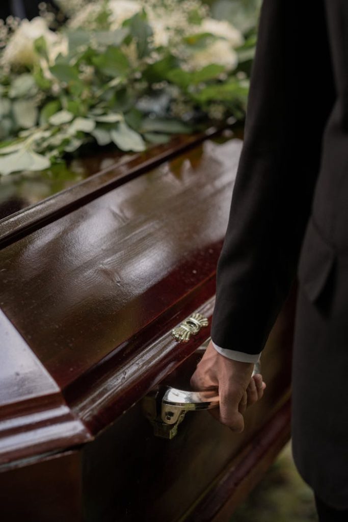 Close-up of a casket with a hand holding the handle during a funeral.