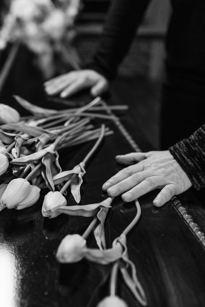 Black and white image of tulips on a coffin with hands, symbolizing loss and sorrow.