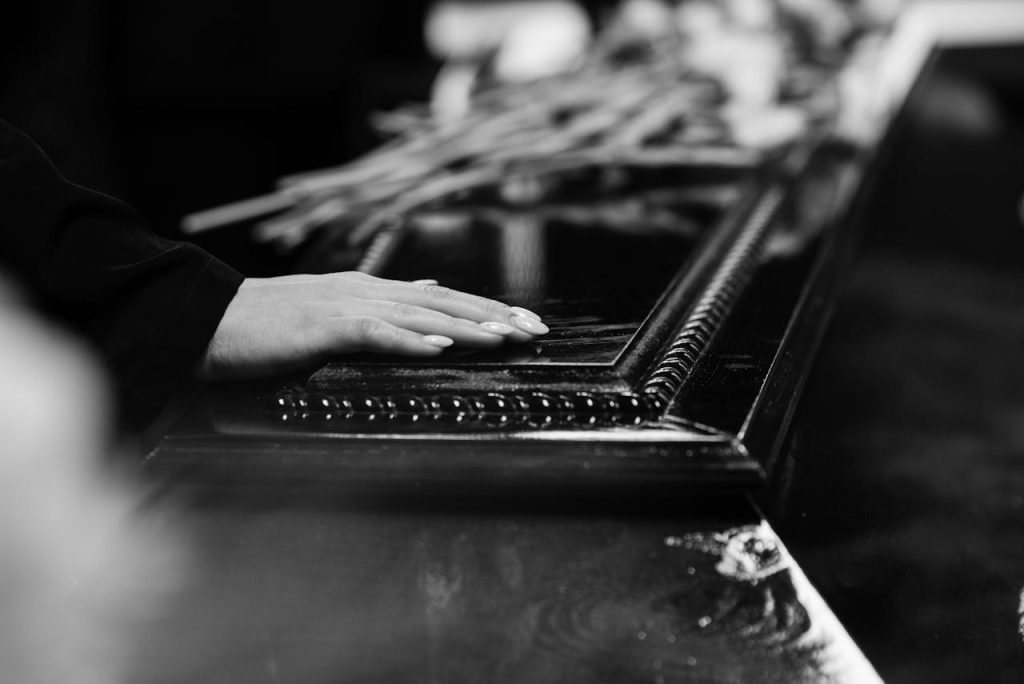 A womans hand rests on a casket, conveying a poignant moment of farewell during a solemn funeral.