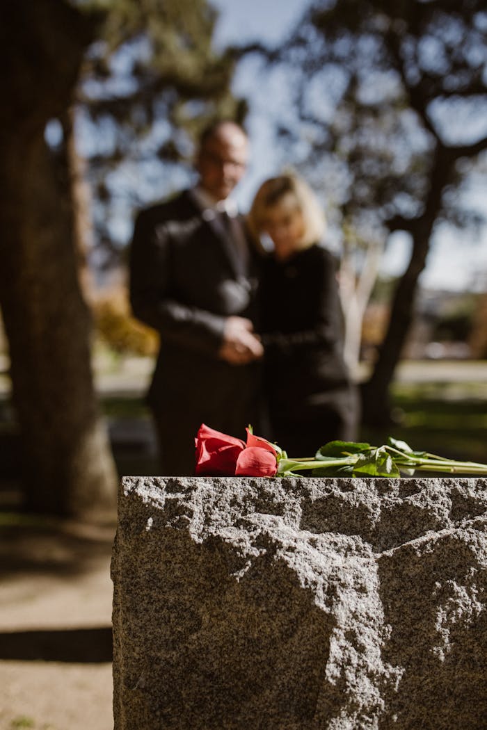 A couple stands in reflection at a gravestone, symbolizing remembrance.